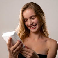 Thumbnail for Smiling woman opening a gift box, excited about the Timeless Photo Necklace by Brother & Sisters.