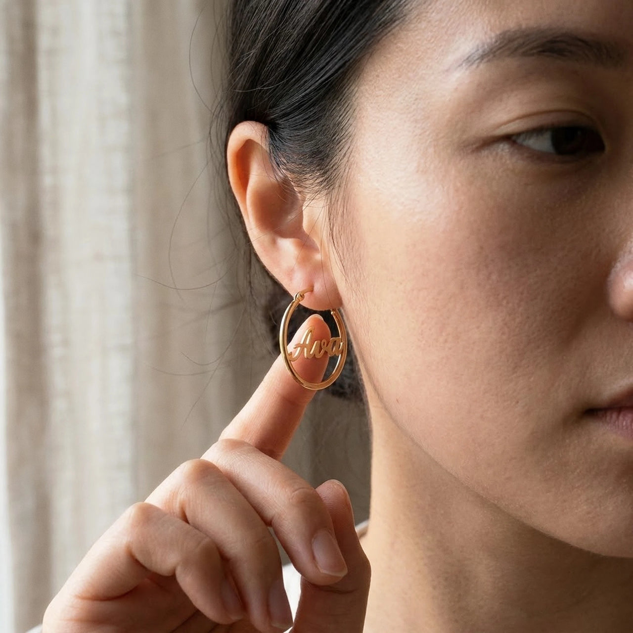 Custom Name Hoop Earrings in Gold held between the fingertips, scale reference | SKU: name-hoop-gold-30-mm