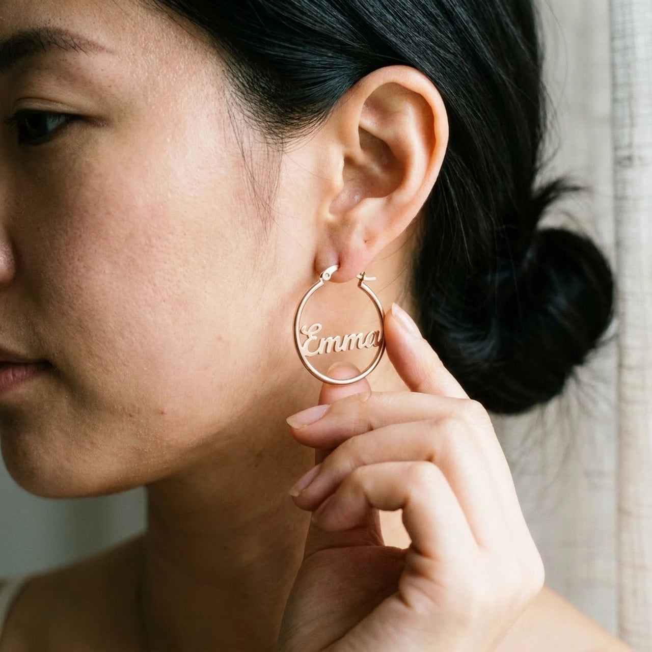 Custom Name Hoop Earrings in Rose Gold held between the fingertips, scale reference | SKU: name-hoop-rose-gold-30-mm
