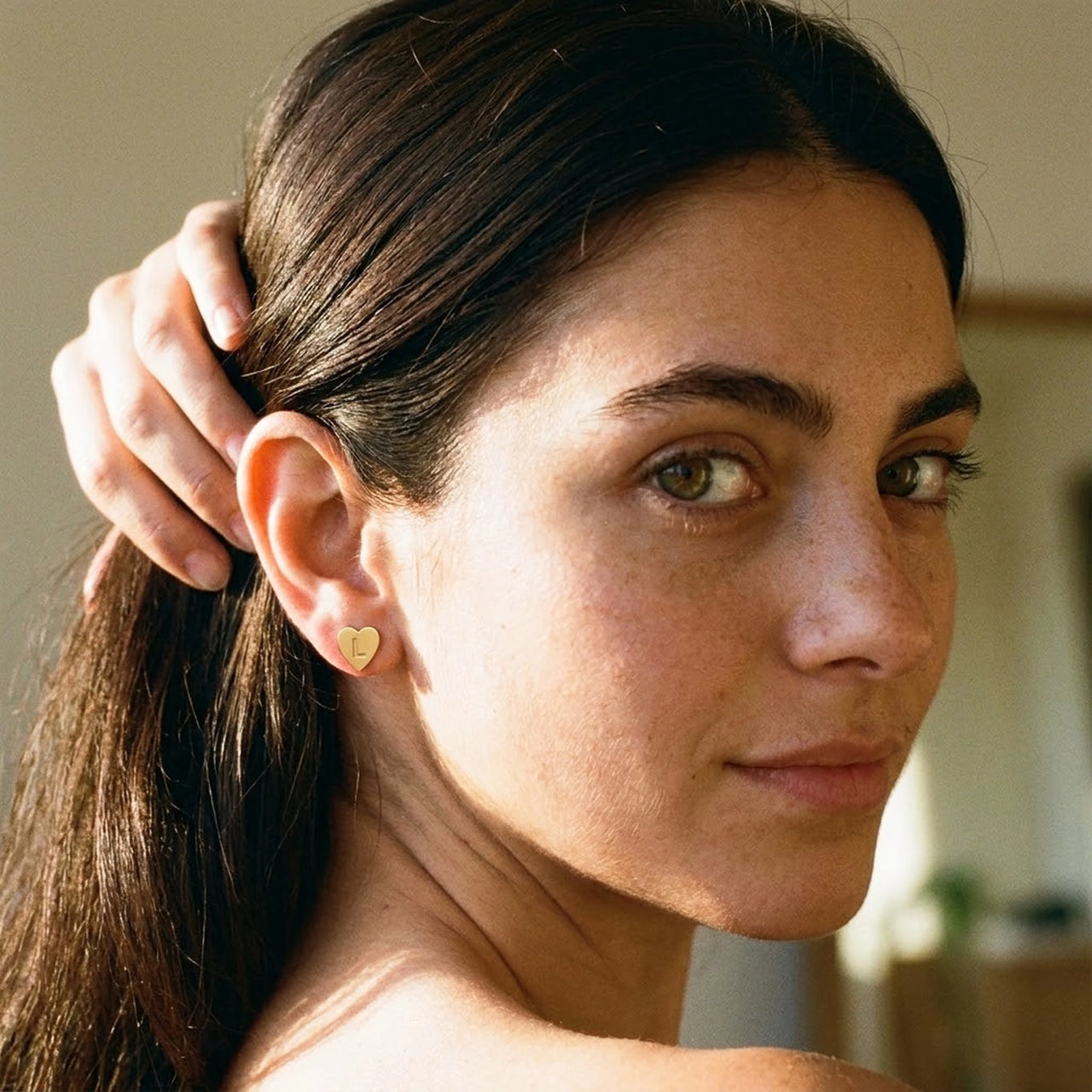Heart Initial Stud Earrings in Gold worn on the ear, close-up on a model | SKU: heart-initial-gold-a