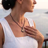 Thumbnail for Woman in a white top by the sea, hand on her heart, wearing the black secret clover photo necklace | SKU: TPH-CLVN-BLACK