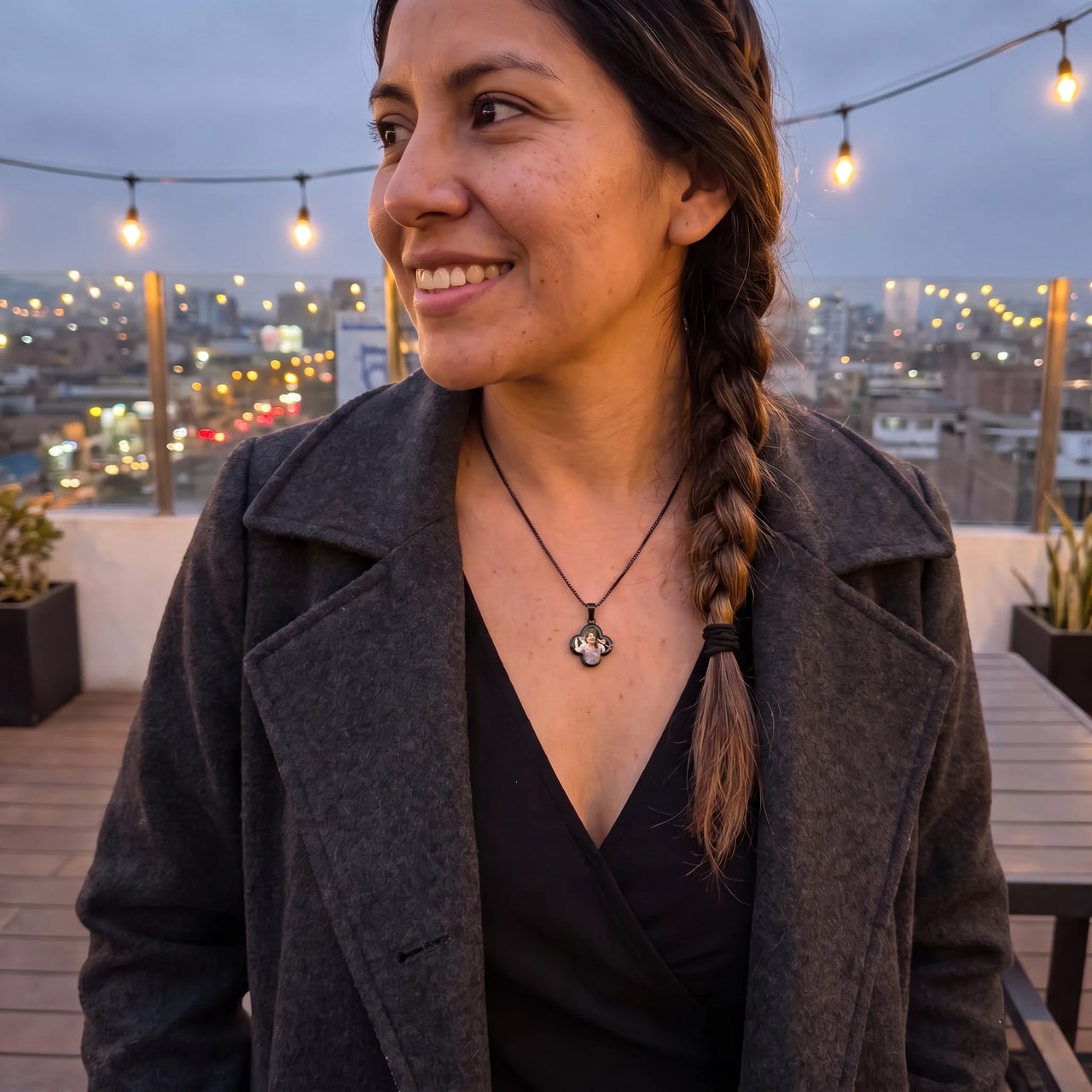 Smiling woman with a braid in a grey coat on a rooftop at dusk, wearing the black secret clover photo necklace | SKU: TPH-CLVN-BLACK