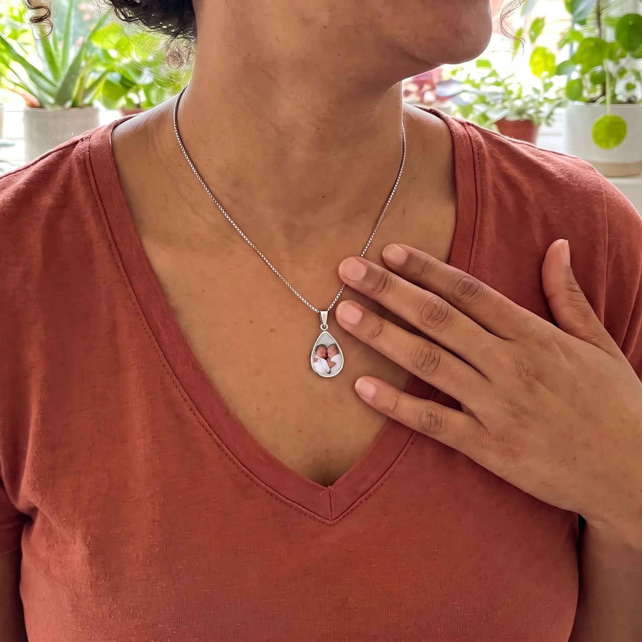 Woman in a rust top with her hand on her heart, wearing the silver secret drop photo necklace | SKU: TPH-DRPN-SILVER